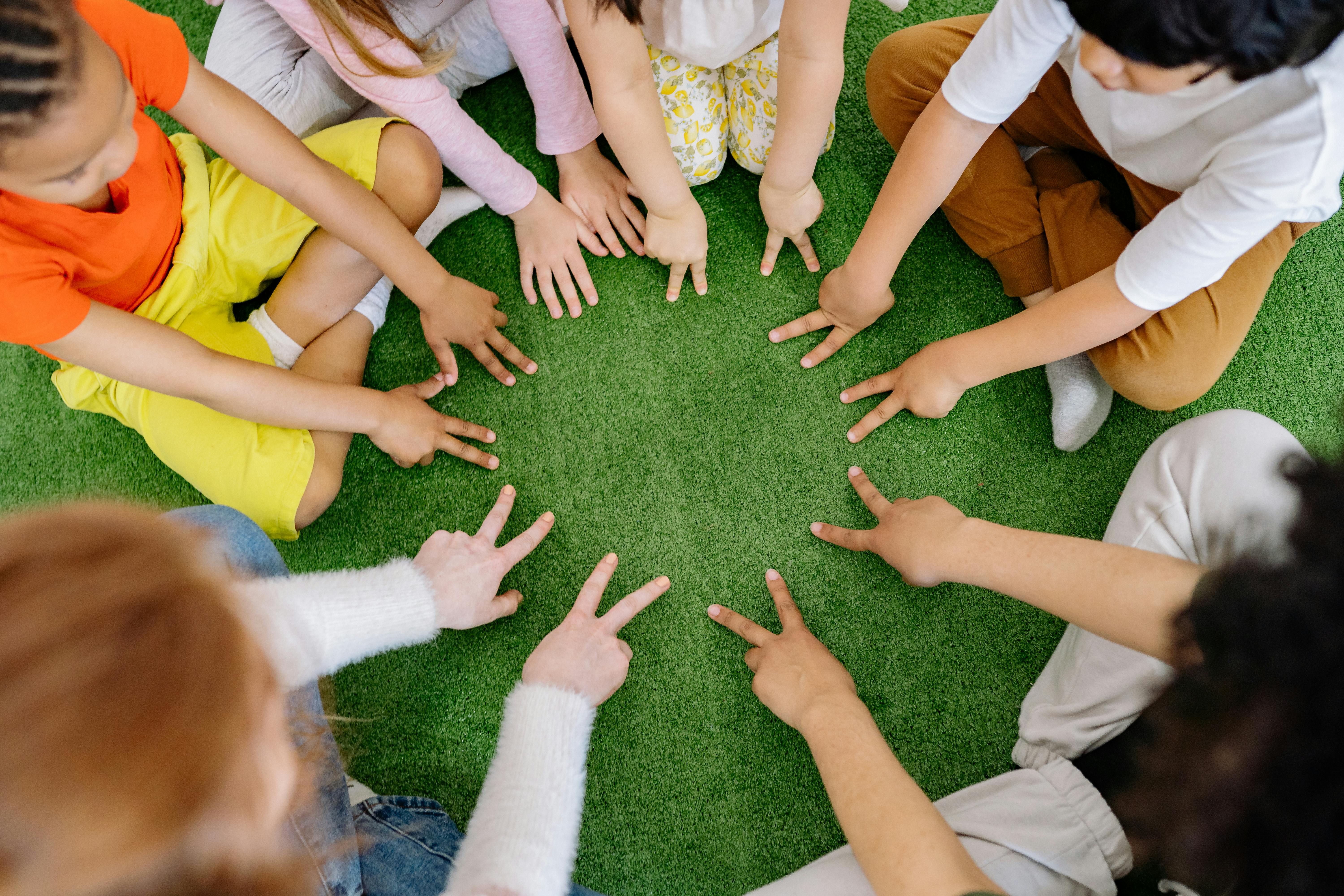 Children reaching hands together in a circle on the grass